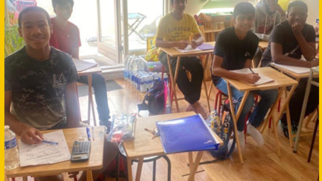 The studio mid-session  a young builder at a laptop, mentor leaning in, others working nearby